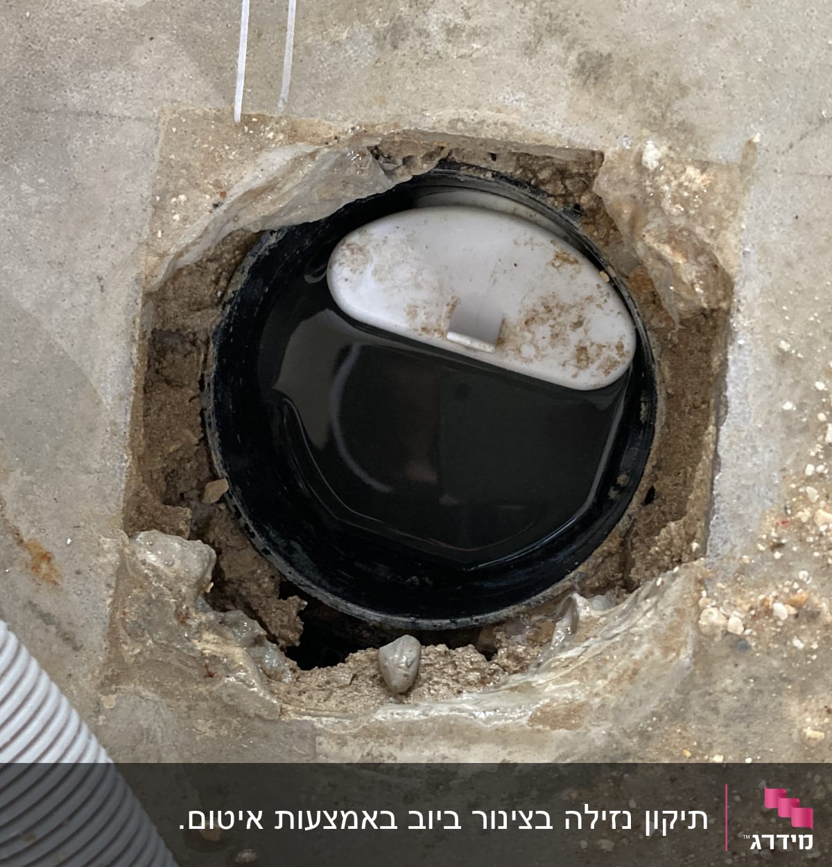פתח ביוב עם מכסה לבן וסביבו צינור גמיש
